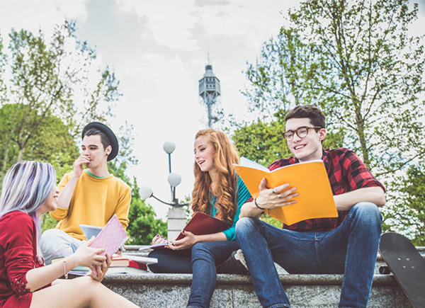 Das Bild zeigt vier junge Studenten, die im Freien auf einer Treppe sitzen und gemeinsam lernen oder sich unterhalten.